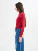 Polera de cuello alto confeccionada en tela rib color blanco, con mangas largas y hombreras. Presenta pespuntes en contraste en las terminaciones del cuello, hombros y puños.