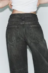 Jeans de tiro alto con diseño de pierna ancha y corte extra largo. Presenta una cintura cruzada asimétrica con cierre de cremallera y botones metálicos, además de un diseño clásico de cinco bolsillos.