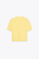 Chaqueta de punto color amarillo pálido, con cuello redondo, manga corta, cierre frontal con botones dorados y bolsillos de parche en el pecho.