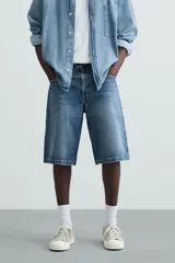 Bermuda de denim de algodón, color azul medio lavado, de corte ancho (baggy fit) y largo hasta la rodilla. Presenta cinco bolsillos y cierre frontal con cremallera y botón.