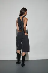 Bermuda de denim negro con diseño holgado, tiro medio y detalles de tachas y strass aplicados en los bolsillos delanteros. Presenta terminaciones deshilachadas en las piernas.