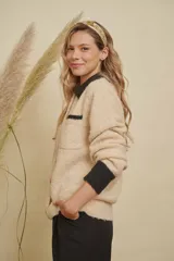 Saco de punto color beige con cuello, puños y detalle de bolsillo en color negro. Presenta cierre frontal con botones dorados y diseño de corte holgado.