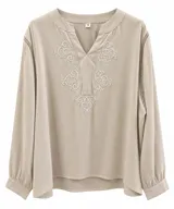 Blusa color beige con escote en V, mangas largas abullonadas y puños con botones. Presenta delicados bordados blancos en el frente y detalles de encaje en las costuras de los hombros.