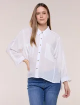 Camisa blanca de silueta holgada y textura liviana, con cuello camisero clásico, abotonadura frontal con botones en contraste y doble bolsillo de parche en el frente. Cuenta con mangas de corte dolman de largo tres cuartos con puño amplio y ruedo recto con aberturas laterales.