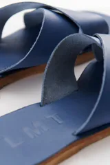Sandalias bajas de cuero azul con tiras anchas cruzadas sobre el empeine y suela plana color madera.