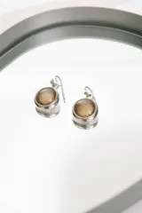 Aros colgantes de plata con piedra redonda translúcida de tono marrón claro y gancho pasante.