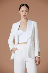 Saco tipo blazer de Natalia Antolín, color blanco, con solapas de satén en contraste, cierre frontal con un botón y detalle de parche con logo en la manga.