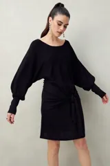 Vestido corto color dorado de punto con brillo integrado en la trama. Diseño de mangas amplias, falda ajustada y lazo frontal que acentúa la cintura.