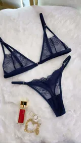 Conjunto de lencería de cuatro piezas en encaje azul marino. Incluye bralette con breteles regulables y cierre frontal, tanga colaless regulable, chaleco de encaje y portaligas con ligas ajustables.