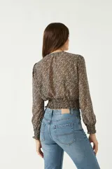 Blusa de manga larga con estampado floral pequeño sobre fondo oscuro. Presenta escote en V con lazo para anudar, cintura con frunce elástico y puños ajustados.