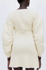 Vestido corto de punto acanalado con cuello redondo, hombros caídos y mangas largas de gran volumen con diseño curvado. Presenta un ajuste entallado en el cuerpo y falda con ligero vuelo.