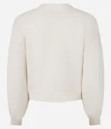 Cardigan corto de punto color beige claro, con escote en V, manga larga abullonada y cierre frontal de botones. Posee bolsillos delanteros tipo parche.