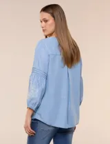 Blusa de tencel celeste con escote cuadrado, mangas tres cuartos abullonadas con puños elastizados y delicados bordados florales blancos en el frente y las mangas.