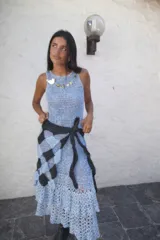 Vestido midi tejido a crochet en color celeste, con diseño de escote redondo y falda con volados en el ruedo. Incluye un cinturón de tejido oscuro con patrón de cuadros atado a la cintura.