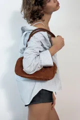 Bolso de hombro de formato alargado confeccionado en gamuza color marrón. Cuenta con doble asa de hombro y cierre superior mediante cremallera metálica.