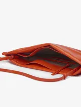 Bolso de mano acolchado de efecto charol color naranja quemado, con forma rectangular y asa larga ajustable y extraíble. Presenta un cierre magnético y el logo grabado en la parte inferior central.