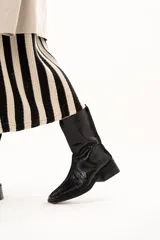 Bota de caña media color negro con textura de reptil, confeccionada en cuero. Presenta horma cuadrada, cierre lateral interno, taco cuadrado y una pequeña plataforma.