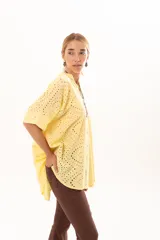 Camisa de corte oversize confeccionada en tela bordada con diseño calado, color amarillo. Presenta cuello mao, cierre frontal con botones y mangas cortas amplias.