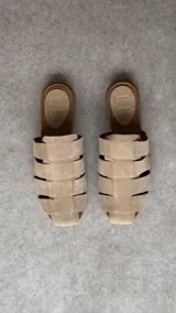 Zuecos de punta cuadrada, confeccionados en gamuza beige con diseño de tiras entrelazadas tipo huarache y suela plana marrón.