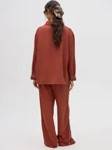 Pantalón de corte holgado y tiro alto con caída recta, color azul petróleo. Presenta una franja lateral decorativa en tonos rojo y amarillo que recorre la pierna, a juego con la camisa de la misma línea.