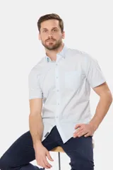 Camisa lisa de manga corta color crema, confeccionada en 100% algodón, con cuello abotonado y un bolsillo en el pecho.