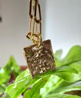 Collar de plata con medalla rectangular texturizada e incrustaciones de cristales verdes, suspendido de una cadena de eslabones.