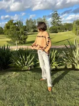 Buzo tejido de punto color beige, con diseño estampado de un caballo y rombos en la parte superior trasera. Presenta cuello redondo, mangas largas y corte holgado.