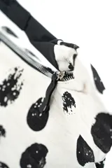 Cartera estilo hobo de color crudo con estampado de manchas negras abstractas, cierre superior y correa de hombro ajustable de cuero negro.