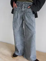 Pantalón wide leg de tiro medio confeccionado en denim blanco. Presenta una cintura con diseño de pasacintas entrelazadas, cierre frontal y bolsillos laterales. Su diseño de pierna amplia ofrece una caída fluida con volumen.