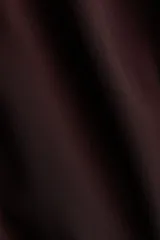 Vestido oversized corto de color marrón oscuro, con escote en V pronunciado y pañuelo haciendo juego que puede abrocharse en la nuca. Cuenta con botones forrados adelante, cinturón fino para atar, mangas globo largas de corte raglán con elástico en los puños y ribete de volados en el bajo.
