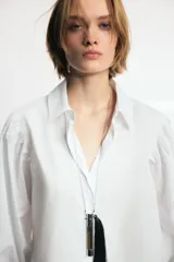 Camisa de cuello solapa y manga larga abullonada con puños abotonados. Presenta un diseño de corte recto con cierre frontal oculto por solapa.