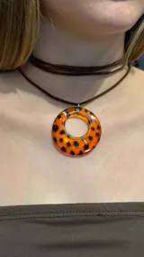 Gargantilla tipo choker con cordón fino de gamuza marrón y dije circular de resina con estampado de carey en tonos naranja y negro.