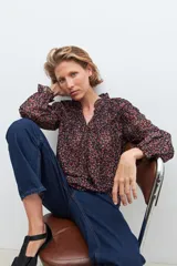 Blusa negra con estampado floral en tonos rosados y rojos, cuello con volados y mangas largas con puños elásticos.