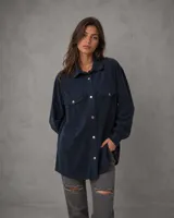 Camisa de pana azul marino con corte oversize, cuello clásico, cierre frontal con botones metálicos y dos bolsillos con solapa en el pecho.