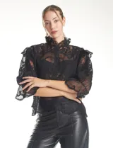 Blusa de tul bordado color negro, con cuello alto, cierre frontal con botones y mangas tres cuartos con terminación amplia.