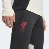 Pantalón de entrenamiento de fútbol Adidas Liverpool FC Tiro 25 Competition, color negro, corte ajustado (slim fit) con puños elásticos y tres franjas verticales rojas en la parte inferior de la pierna. Incluye el escudo del Liverpool FC aplicado con calor en el muslo.