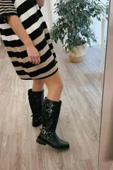 Bota alta de cuero negro con caña alta y hebillas plateadas.