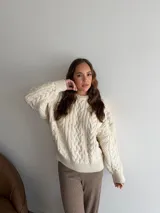 Buzo de punto con diseño de trenzas, color crema, de cuello redondo y manga larga con puños acanalados.