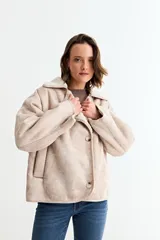 Chaqueta de simil gamuza en color beige, con forro interno y cuello de corderito sintético. Presenta un diseño de corte holgado, cierre frontal con botones y bolsillos laterales.