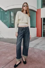 Jeans de mezclilla azul oscuro con efecto desgastado, tiro medio, corte relajado y pernera ancha. Presentan un bajo ancho doblado hacia arriba, revelando el revés del tejido de color beige claro con un detalle de costura amarilla.