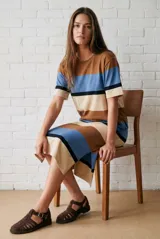 Vestido midi de punto con diseño de rayas horizontales en tonos marrón, azul y beige. Presenta cuello redondo, mangas cortas y un corte recto con aberturas laterales en el ruedo.