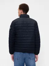 Campera puffer de diseño ligero, color verde militar, con cierre frontal completo y cuello alto. Presenta un acabado acolchado horizontal y puños elásticos.