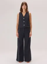 Chaleco negro sin mangas, de corte recto y largo a la cintura, con cuello redondo y cierre frontal oculto.