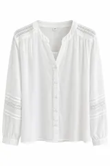 Blusa blanca de manga larga con escote en V y cuello mao. Cuenta con delicados detalles de encaje y frunces en los hombros y las mangas.