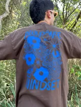 Remera marrón con estampa azul de flores y texto "Abundance is a mindset".