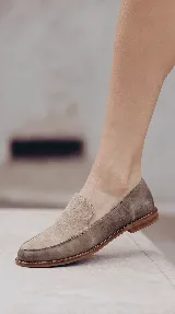 Mocasines de gamuza color tostado, con diseño clásico de pespuntes marcados en la parte delantera y suela plana.