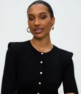 Cardigan de punto color blanco, de corte regular y ajuste al cuerpo. Presenta cuello redondo, mangas largas, cierre frontal con botones delicados y hombreras estructuradas que aportan volumen a la silueta.