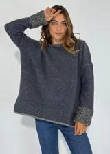 Sweater azul oscuro de corte holgado, con cuello redondo y mangas largas. Los puños y el cuello tienen un detalle de tejido texturizado en tonos grises y beige. El ruedo también presenta un borde en tono gris.