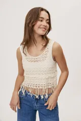 Top sin mangas de crochet color crudo, con escote redondo, diseño calado y terminación con flecos en el ruedo.