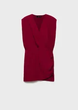 Vestido corto de color rojo, con diseño cruzado, escote en V profundo y hombreras marcadas. Presenta un drapeado lateral en la cintura y falda con corte asimétrico.